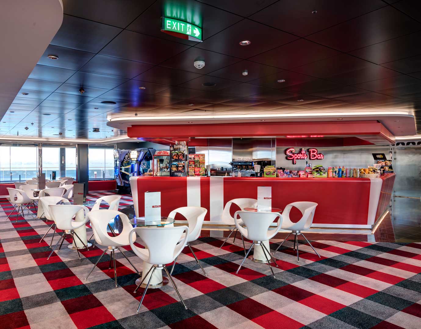 Modern sports bar with red decor, white chairs, and arcade games onboard a cruise ship | MSC Cruises Modern sports bar with red decor, white chairs, and arcade games onboard a cruise ship | MSC Cruises