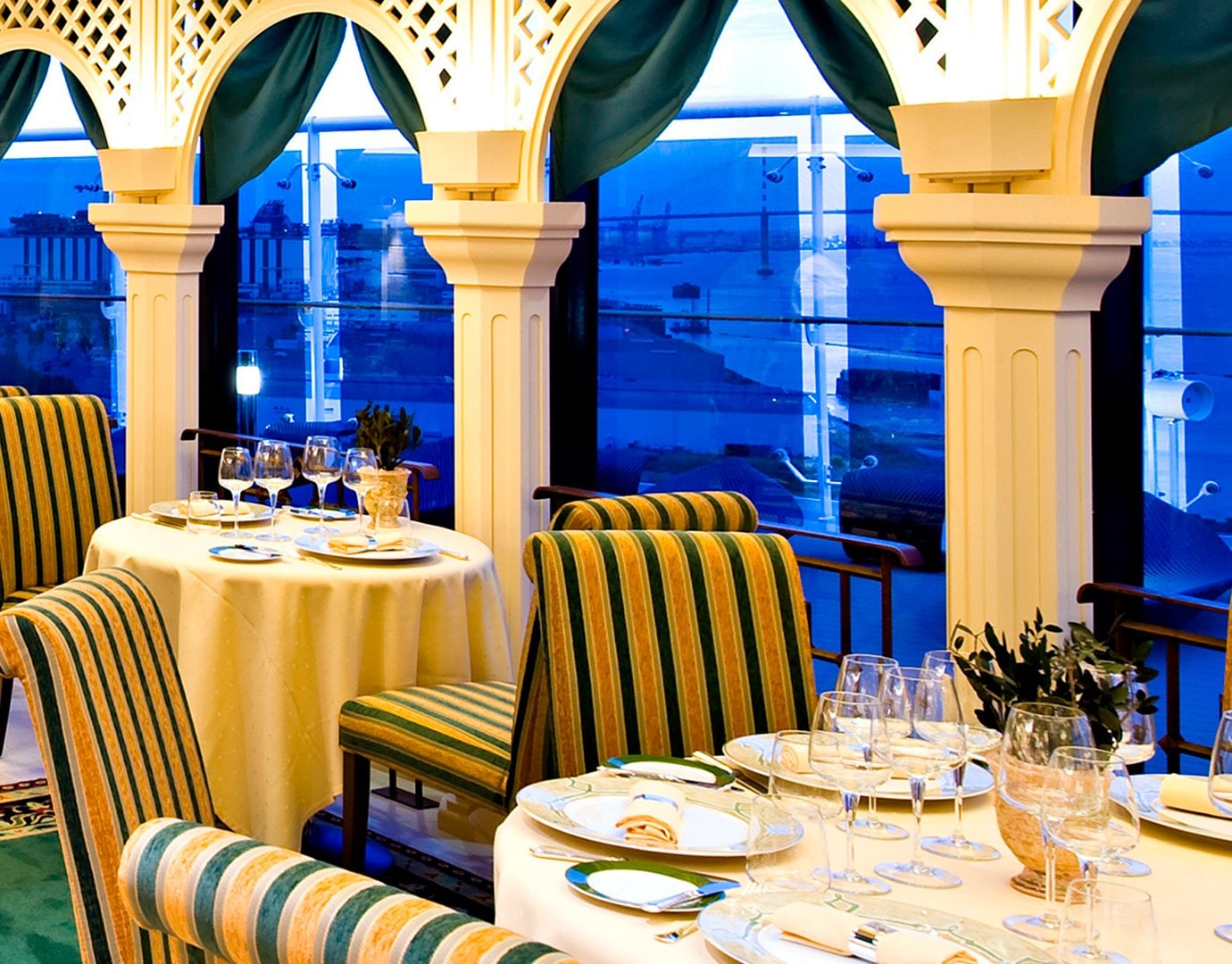 Elegant dining area with striped chairs and ocean views at sunset | MSC Cruises Elegant dining area with striped chairs and ocean views at sunset | MSC Cruises