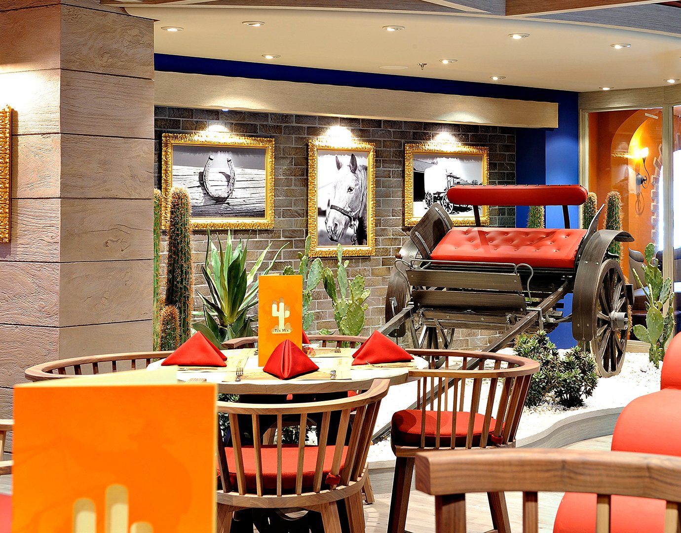 Western-style restaurant decor with a red carriage, cacti, and framed horse-themed art | MSC Cruises Western-style restaurant decor with a red carriage, cacti, and framed horse-themed art | MSC Cruises