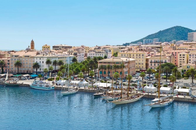 A scenic harbor with sailboats, colorful buildings, and a mountain backdrop in Ajaccio, Corsica | MSC Cruises A scenic harbor with sailboats, colorful buildings, and a mountain backdrop in Ajaccio, Corsica | MSC Cruises