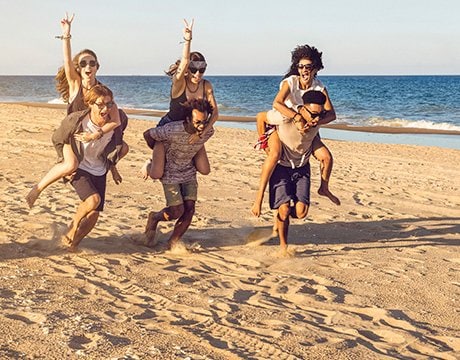 Friends enjoying a playful piggyback race on a sandy beach near the ocean | MSC Cruises Friends enjoying a playful piggyback race on a sandy beach near the ocean | MSC Cruises