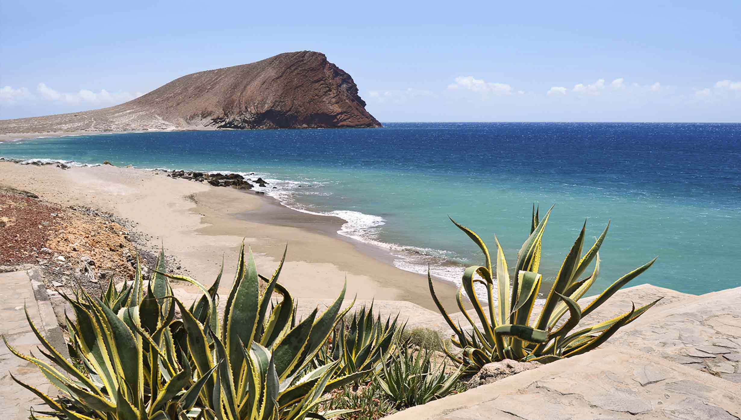A scenic beach with turquoise waters and a rocky hill in the distance | MSC Cruises