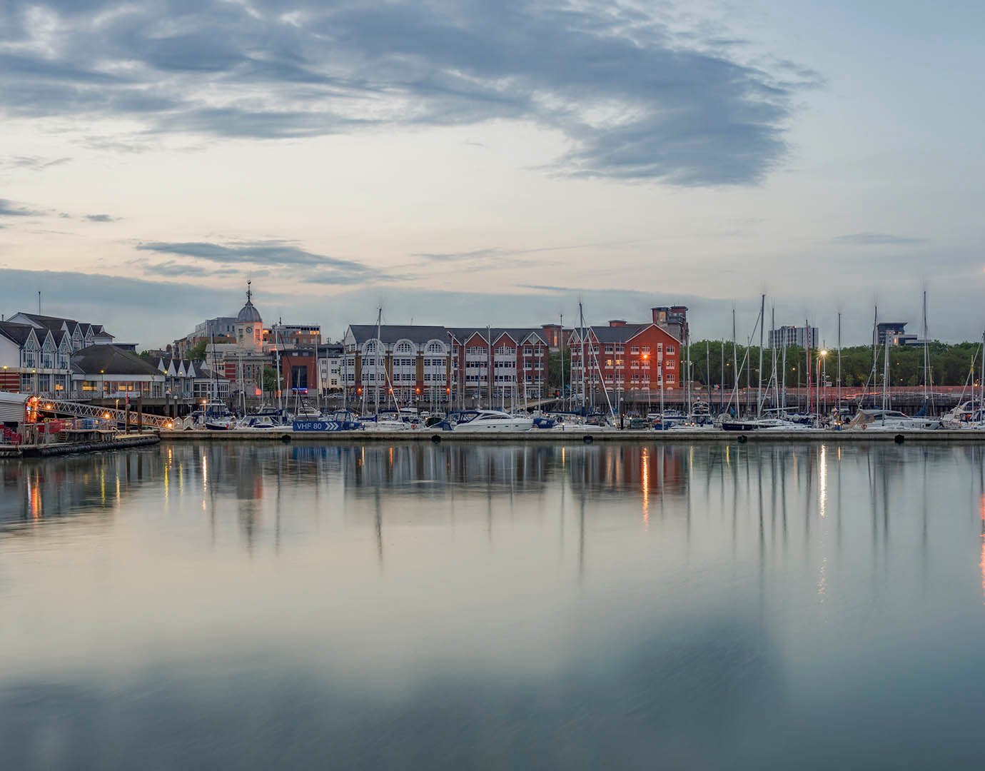 A marina with sailboats and waterfront buildings at dusk | MSC Cruises