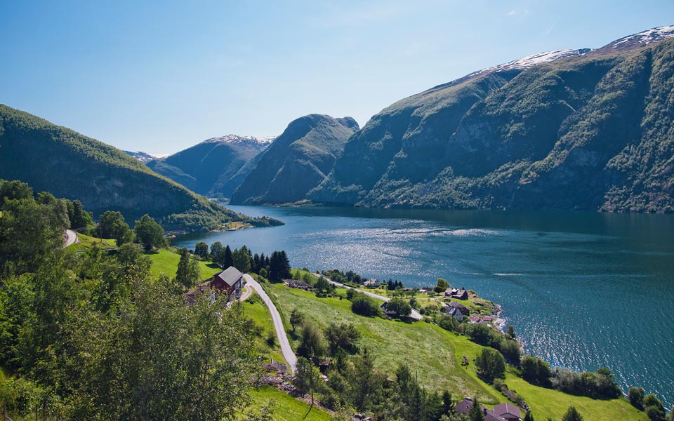 Scenic view of a fjord surrounded by lush green hills and mountains under a clear blue sky | MSC Cruises Scenic view of a fjord surrounded by lush green hills and mountains under a clear blue sky | MSC Cruises