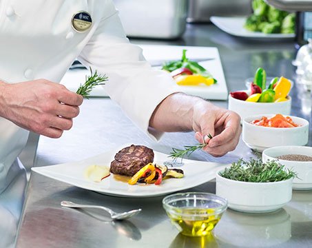 A chef garnishing a gourmet dish with fresh rosemary onboard | MSC Cruises A chef garnishing a gourmet dish with fresh rosemary onboard | MSC Cruises