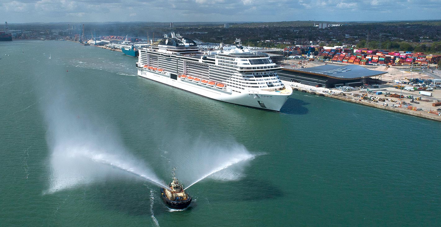 A large MSC cruise ship docked at a modern port with a tugboat spraying water | MSC Cruises