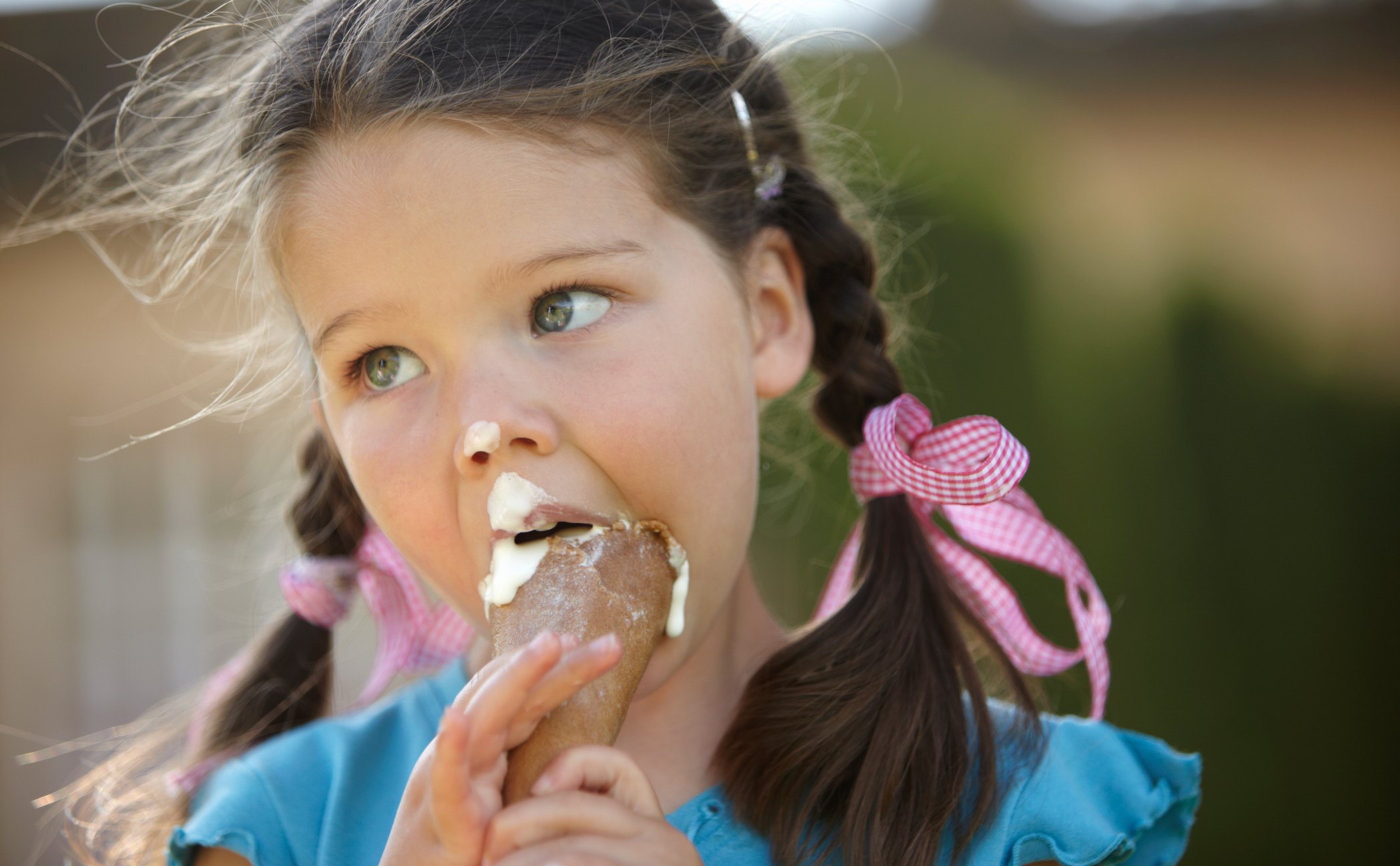 A child enjoying an ice cream outdoors with braided hair and pink ribbons | MSC Cruises