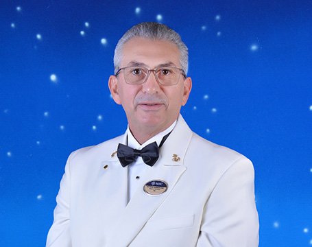 A crew member in a white uniform with an MSC name badge against a starry blue background | MSC Cruises A crew member in a white uniform with an MSC name badge against a starry blue background | MSC Cruises