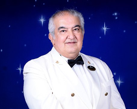 Crew member in a formal white uniform with a starry blue background | MSC Cruises Crew member in a formal white uniform with a starry blue background | MSC Cruises