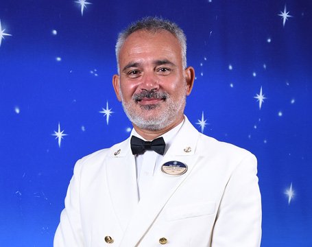 A crew member in a formal white uniform with a starry backdrop | MSC Cruises A crew member in a formal white uniform with a starry backdrop | MSC Cruises
