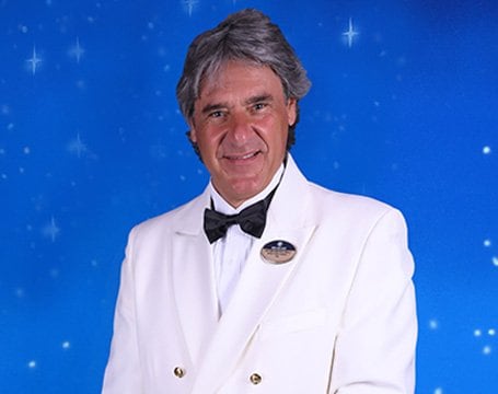 Crew member in a white formal uniform against a starry blue background | MSC Cruises Crew member in a white formal uniform against a starry blue background | MSC Cruises